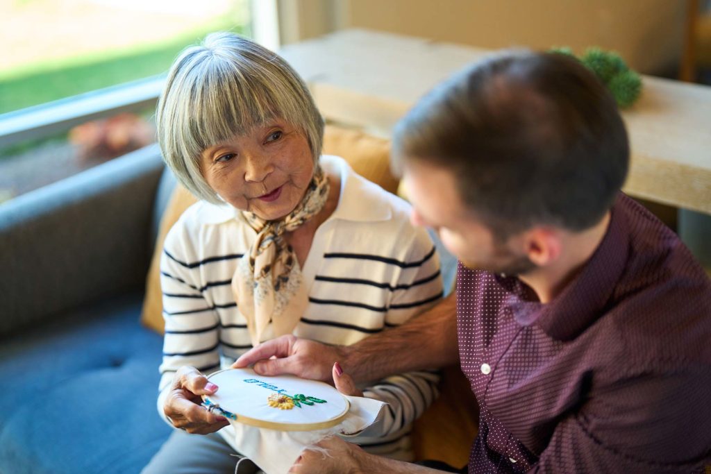 An employee helps an elderly woman with embroidery